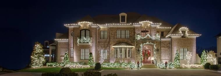 Large brick mansion elaborately decorated with Christmas lights and garland at night